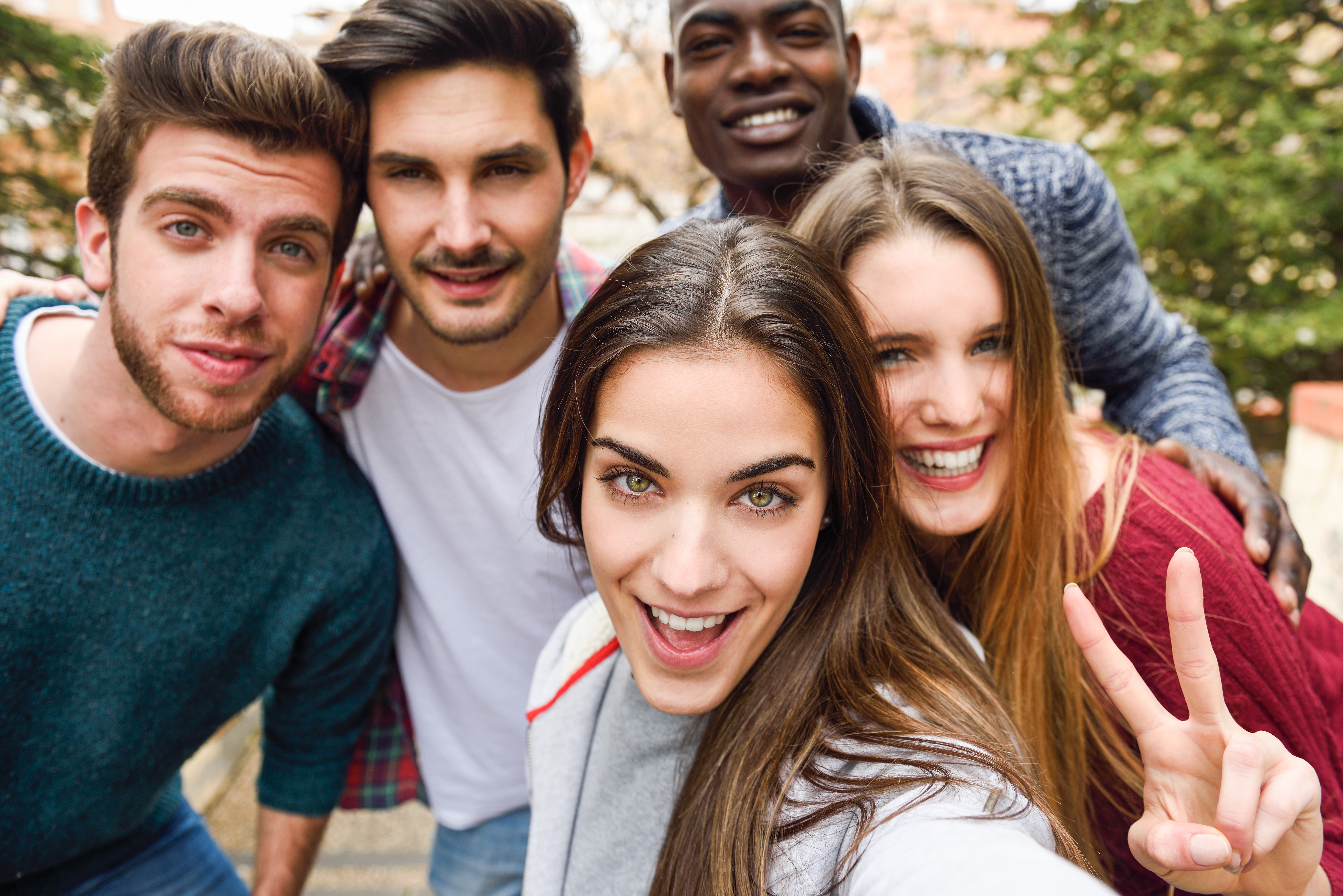  A group of five friends, three men and two women, are taking a selfie together outdoors.