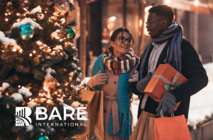 A man and woman holding presents and shopping bags standing beside a Christmas tree