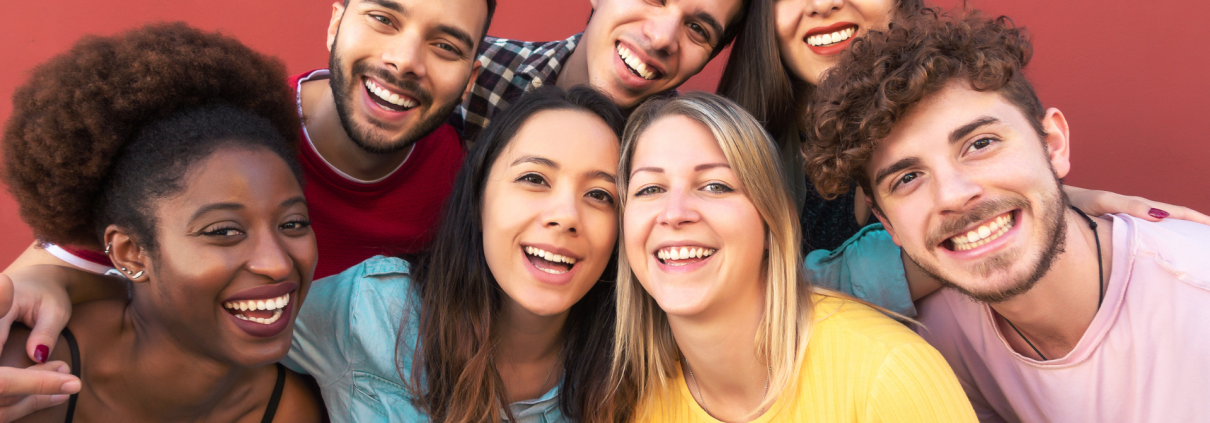 Group of seven smiling, happy individuals against a red background.