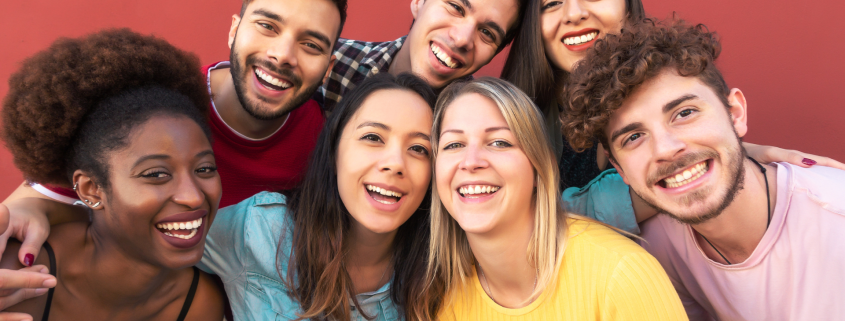 Group of seven smiling, happy individuals against a red background.